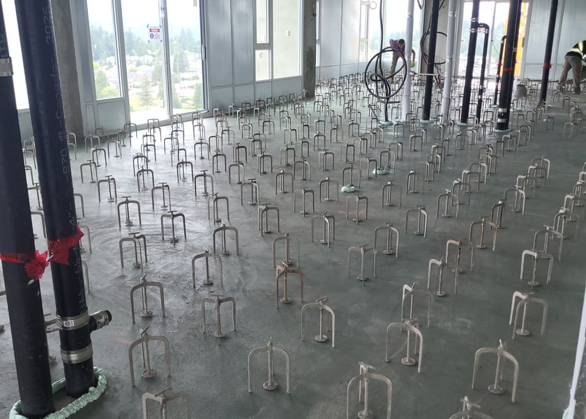 Adjustable leveling pedestals spaced across a bare concrete slab high in a tower, mountain view through the windows