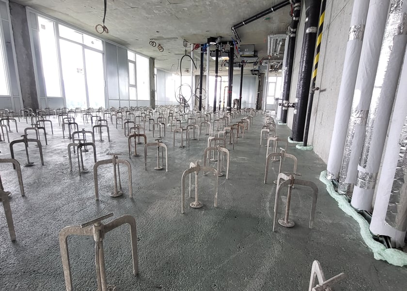 Leveling pedestals spaced across a concrete slab next to insulated pipe risers and hazard tape