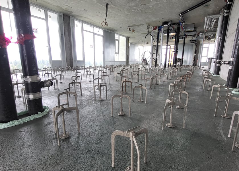 Wide view of leveling pedestals across a concrete slab with black pipe risers running along a window wall