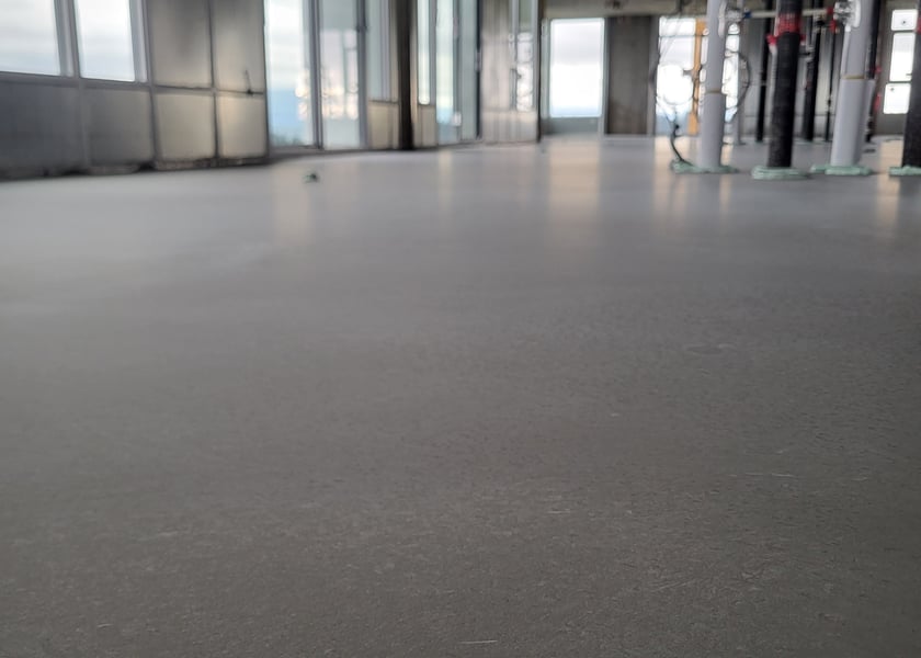 Freshly self-leveled concrete floor with a smooth grey finish, structural columns and floor to ceiling windows in the background
