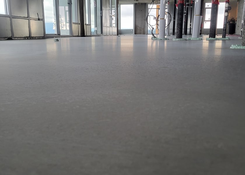 Wide view of a freshly poured self-leveling floor reflecting light near wrapped columns and a window wall