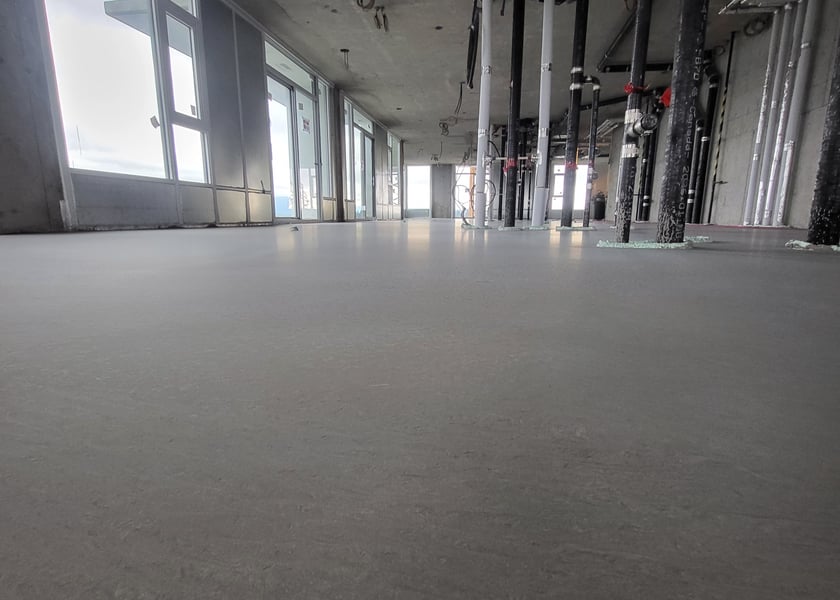 Low angle view of a newly poured self-leveling floor stretching toward a row of columns with pipe risers