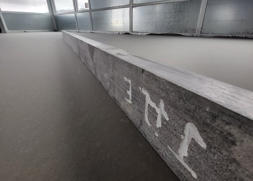 Straightedge tool laid across a self-leveled concrete floor along a window wall to check flatness