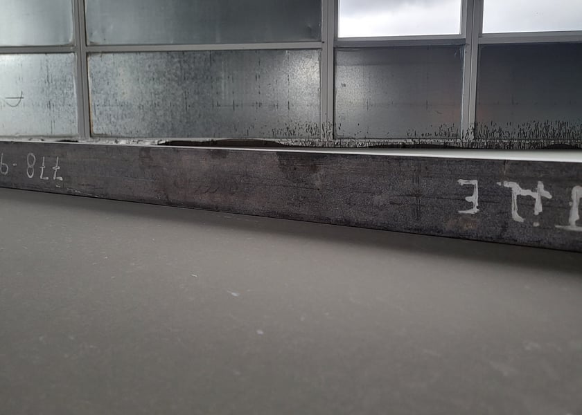 Low angle view of a straightedge tool resting on a concrete floor beneath a window sill