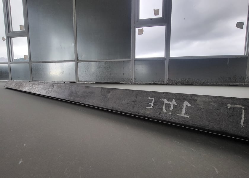 Diagonal view of a straightedge tool laid across a self-leveled concrete floor near a window wall