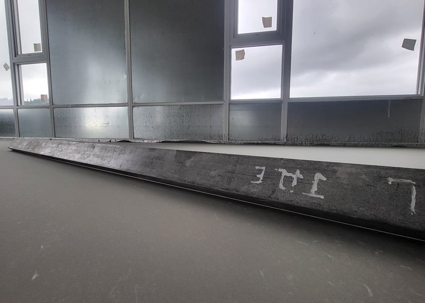 Straightedge tool laid along a window wall on a freshly leveled concrete floor