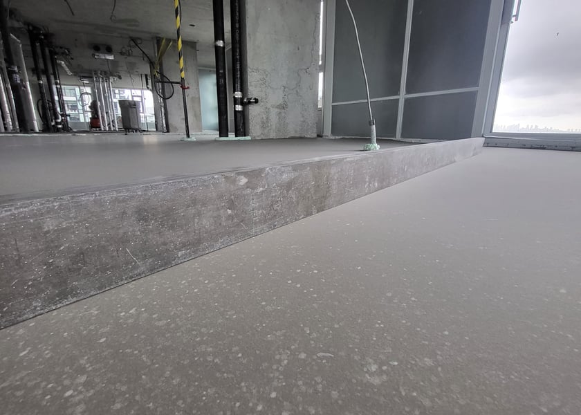 Step edge between an unfinished concrete slab and a newly self-leveled floor, pipes visible in the background