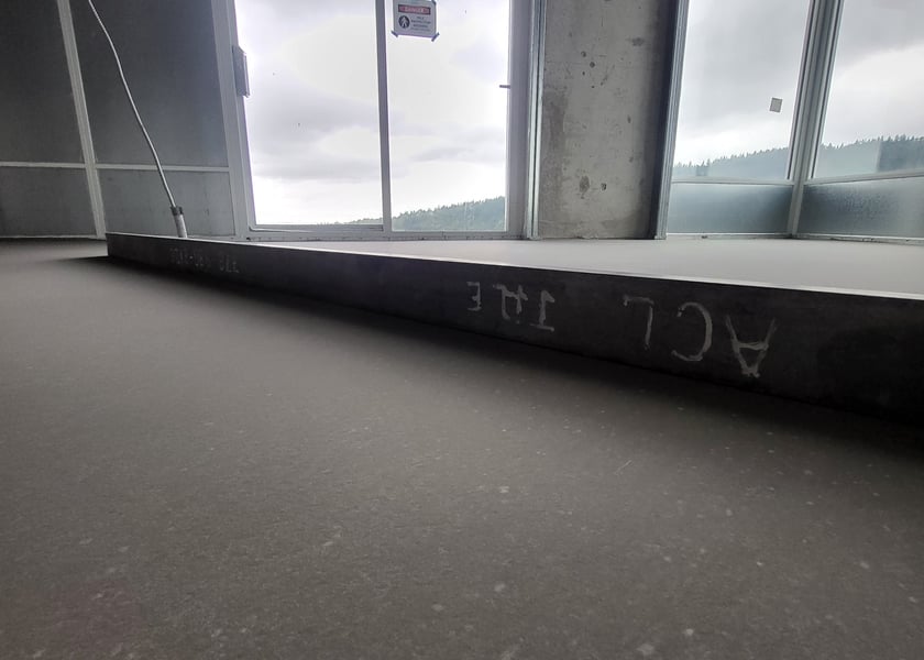 Low angle view of a straightedge tool along a window sill on a self-leveled concrete floor