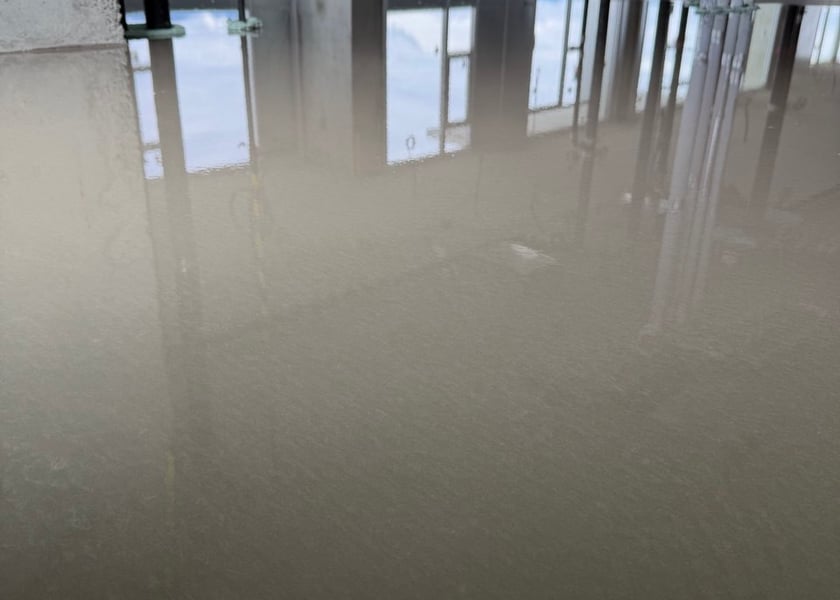 Reflection of ceiling pipes and a window wall in a wet self-leveling floor still curing