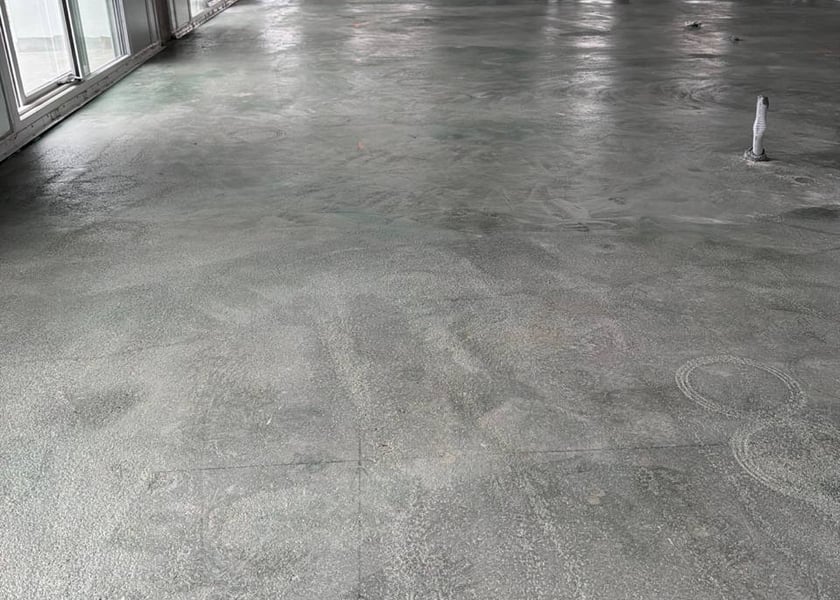 Cured concrete floor with faint circular grinder marks near a window wall