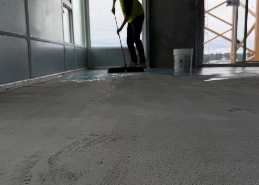 Low angle view of a worker spreading primer along a window wall with a push broom