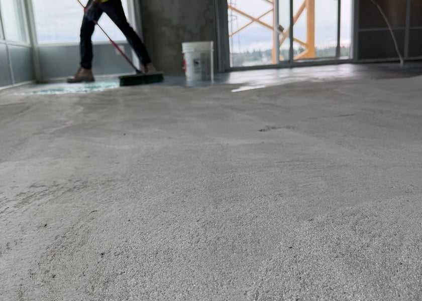 Low angle view of a worker spreading primer along a window wall, a tower crane visible outside