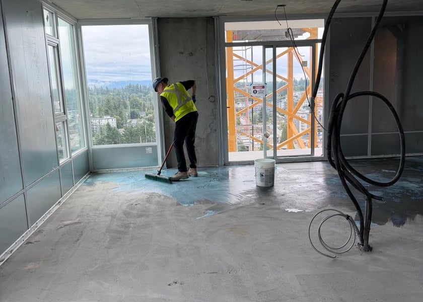 Worker in a safety vest applying primer across a unit floor with a city view through the windows