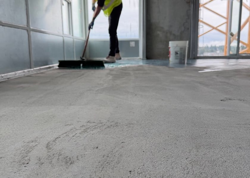 Low angle view of a worker pushing a broom through primer near a window wall