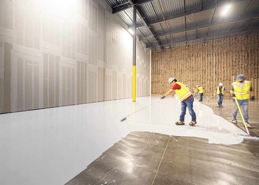 Crew spreading self-leveling compound across a warehouse slab